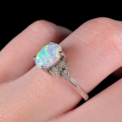 Macro view of women's sterling silver ring with lab-created opal center worn on finger, focusing on illusion-set diamonds in shoulder of ring.