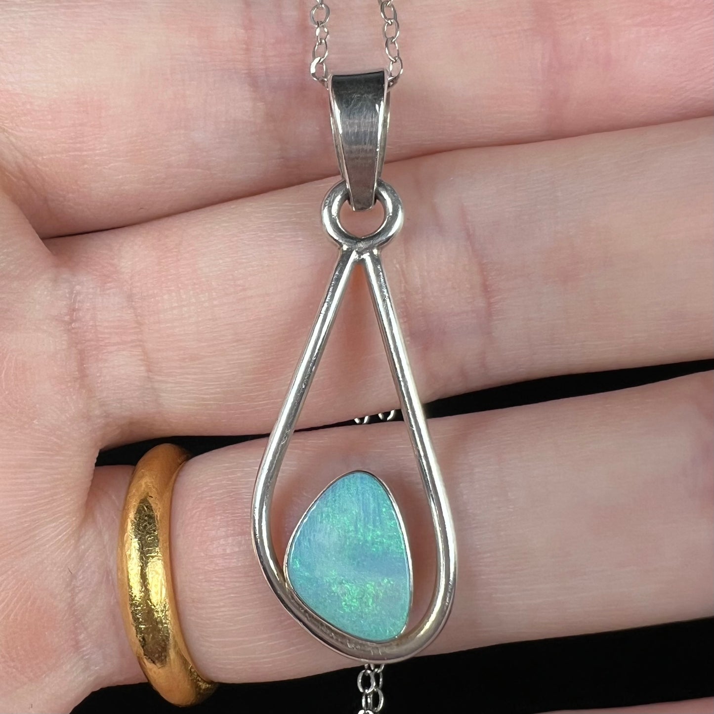 Close-up of a sterling silver women's opal doublet necklace held in a hand under cool studio light.  The opal has soft green fire.