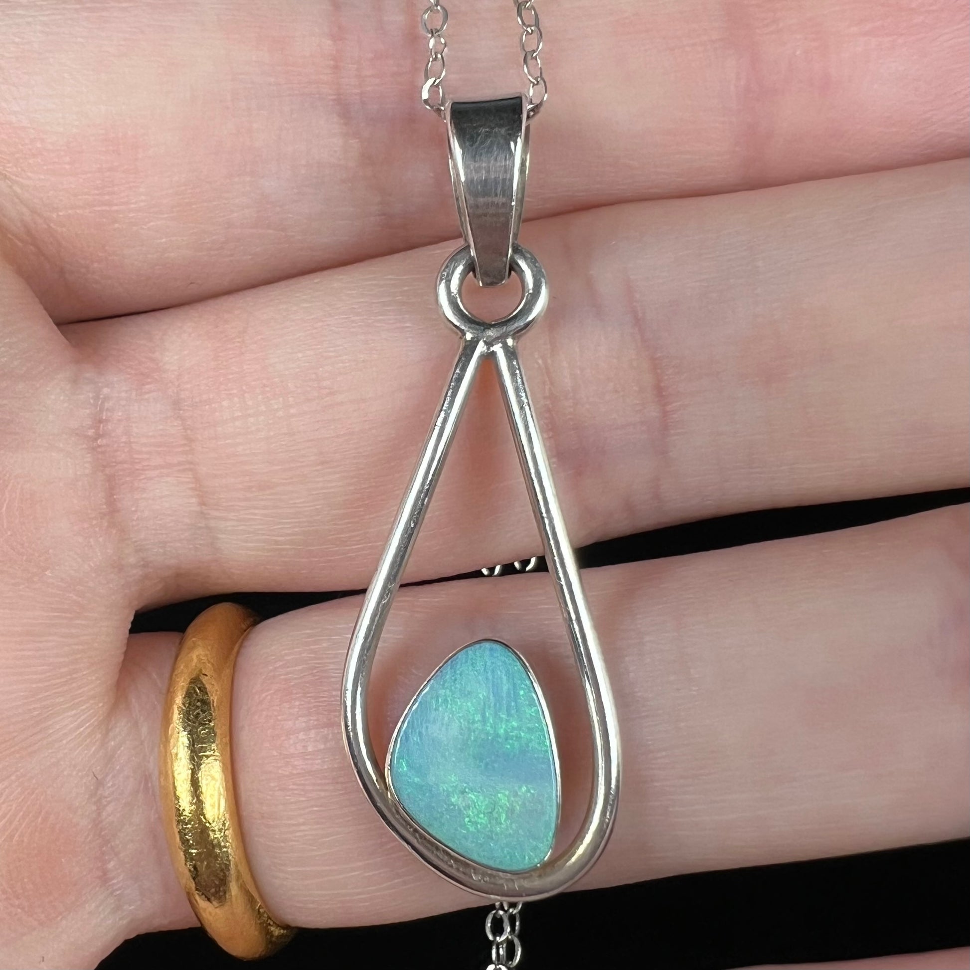 Close-up of a sterling silver women's opal doublet necklace held in a hand under cool studio light.  The opal has soft green fire.