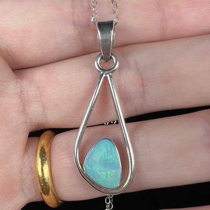 Close-up of a sterling silver women's opal doublet necklace held in a hand under cool studio light.  The opal has soft green fire.