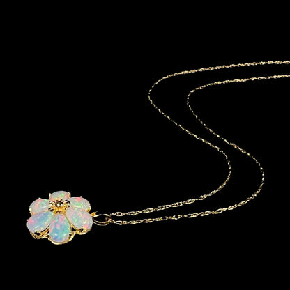 Women's lab-created opal flower necklace in 14k gold shown from angle laying on black background, its chain trailing behind the pendant