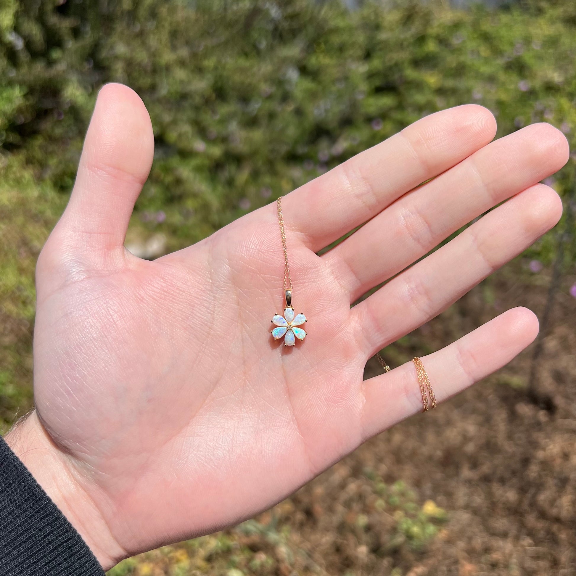 Hand holding women's opal flower necklace in hand under natural sunlight