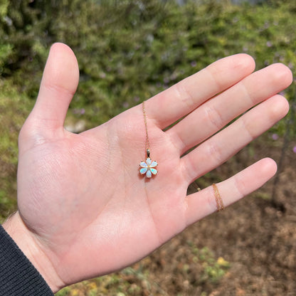 Hand holding women's opal flower necklace in hand under natural sunlight