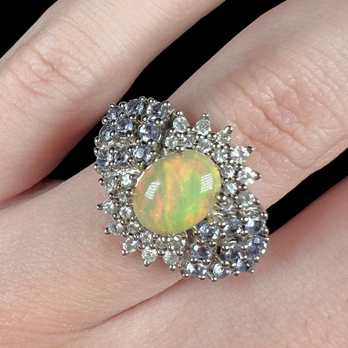 Close-up of women's fire opal and gemstone cluster ring, worn on finger