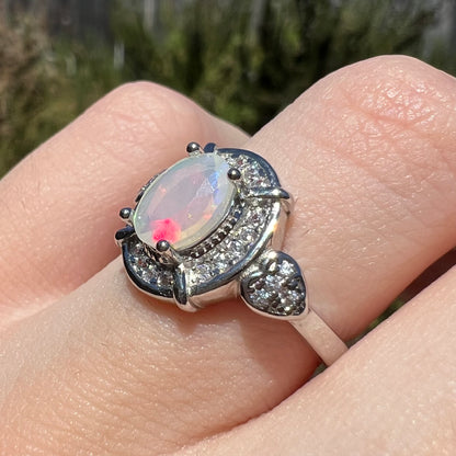 CZ-accented heart design showing on women's sterling silver opal ring, worn on finger in sunlight