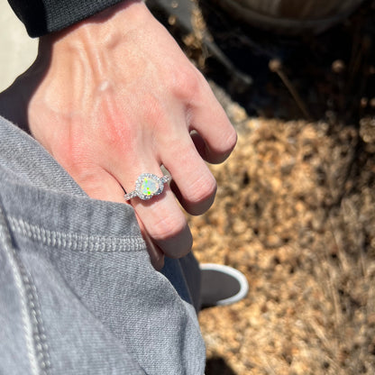 Person's hand resting on their hip wearing women's sterling silver opal heart design ring in sunlight