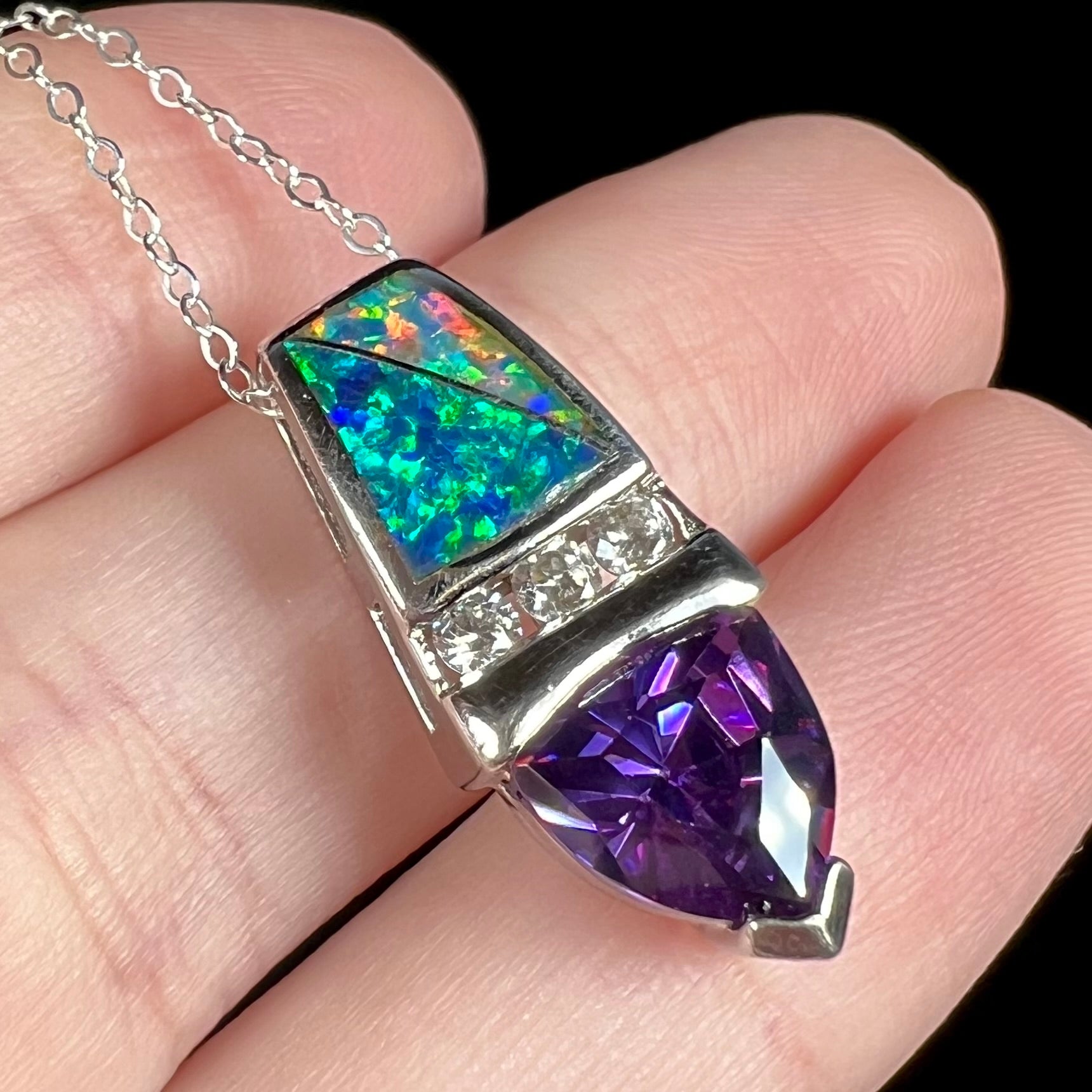 Angled macro close-up of a women's lab-created opal inlay and purple trillion cut stone pendant in sterling silver, resting on fingers.