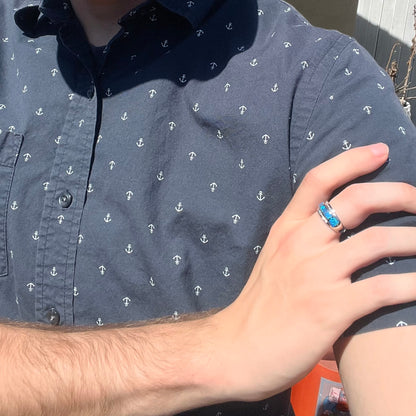 Close-up of person resting hand on opposing shoulder in sunlight wearing a women's blue Australian opal inlay ring with diamond accents in white gold
