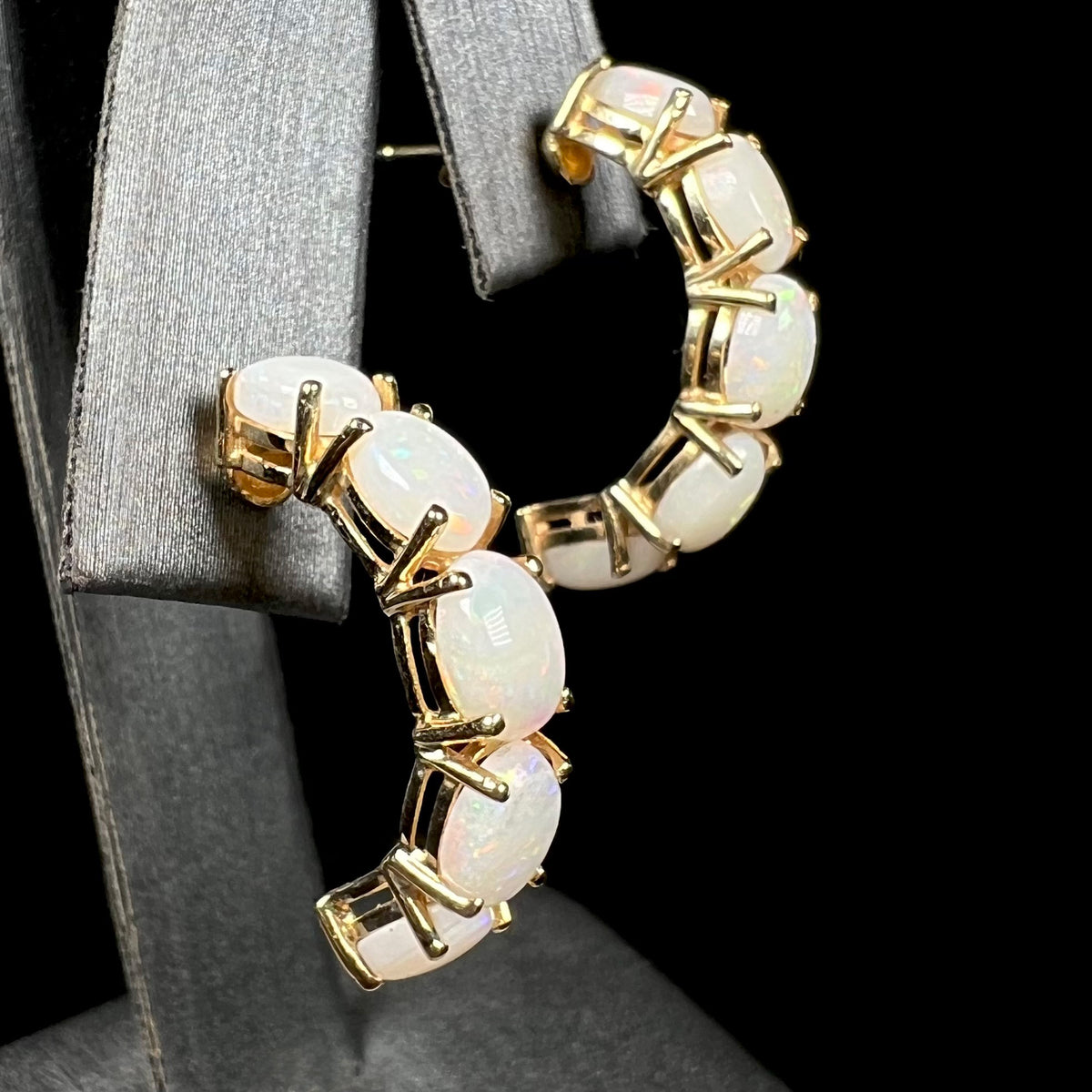 Pair of women's gold Australian white opal semi-hoop earrings shown close-up from side angle on earring display