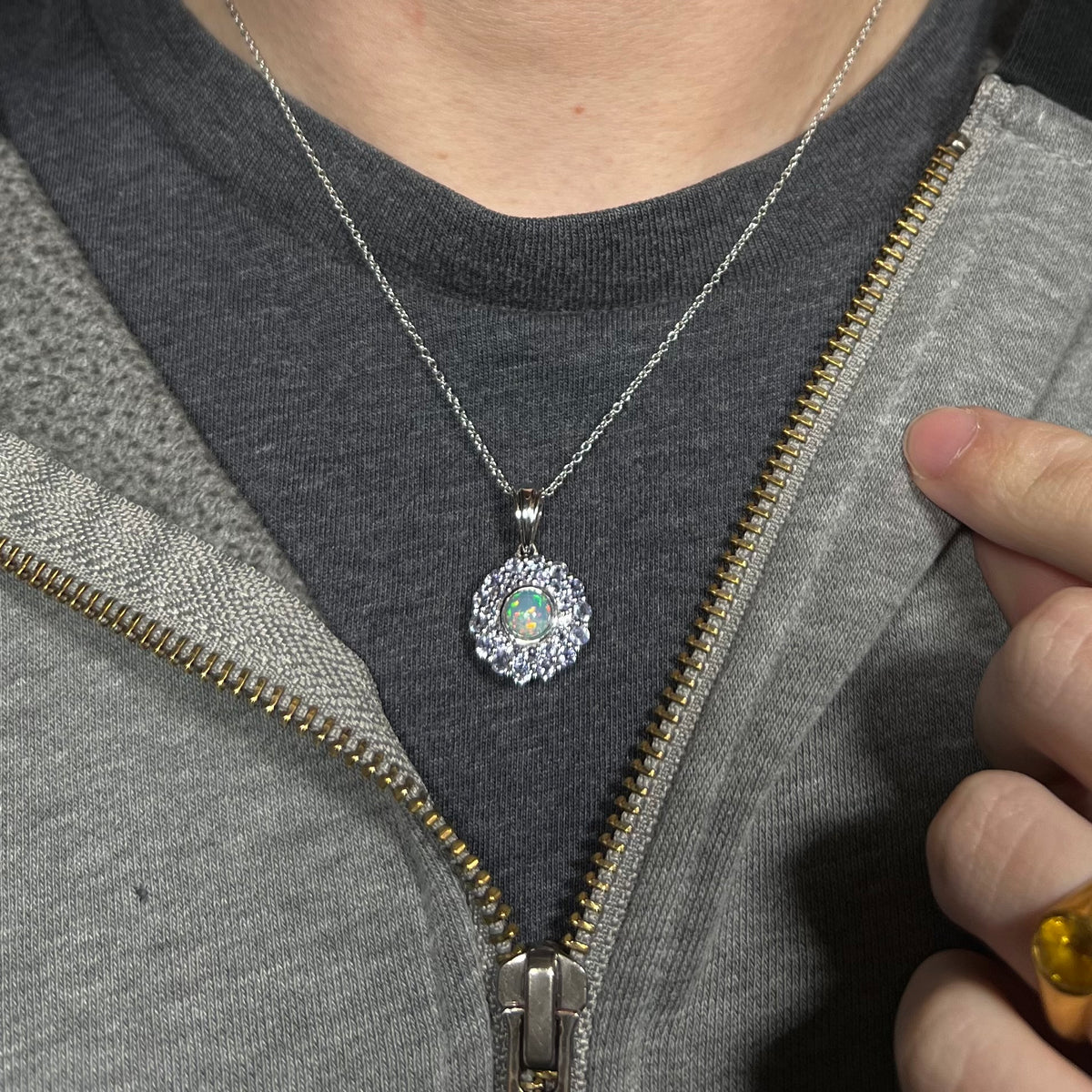 Close-up of person wearing a women's sterling silver opal and tanzanite halo necklace around their neck against a dark shirt beneath a hoodie.