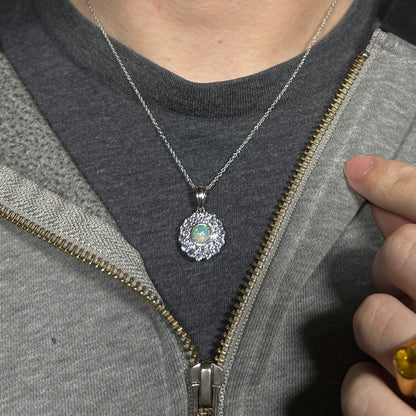 Close-up of person wearing a women's sterling silver opal and tanzanite halo necklace around their neck against a dark shirt beneath a hoodie.