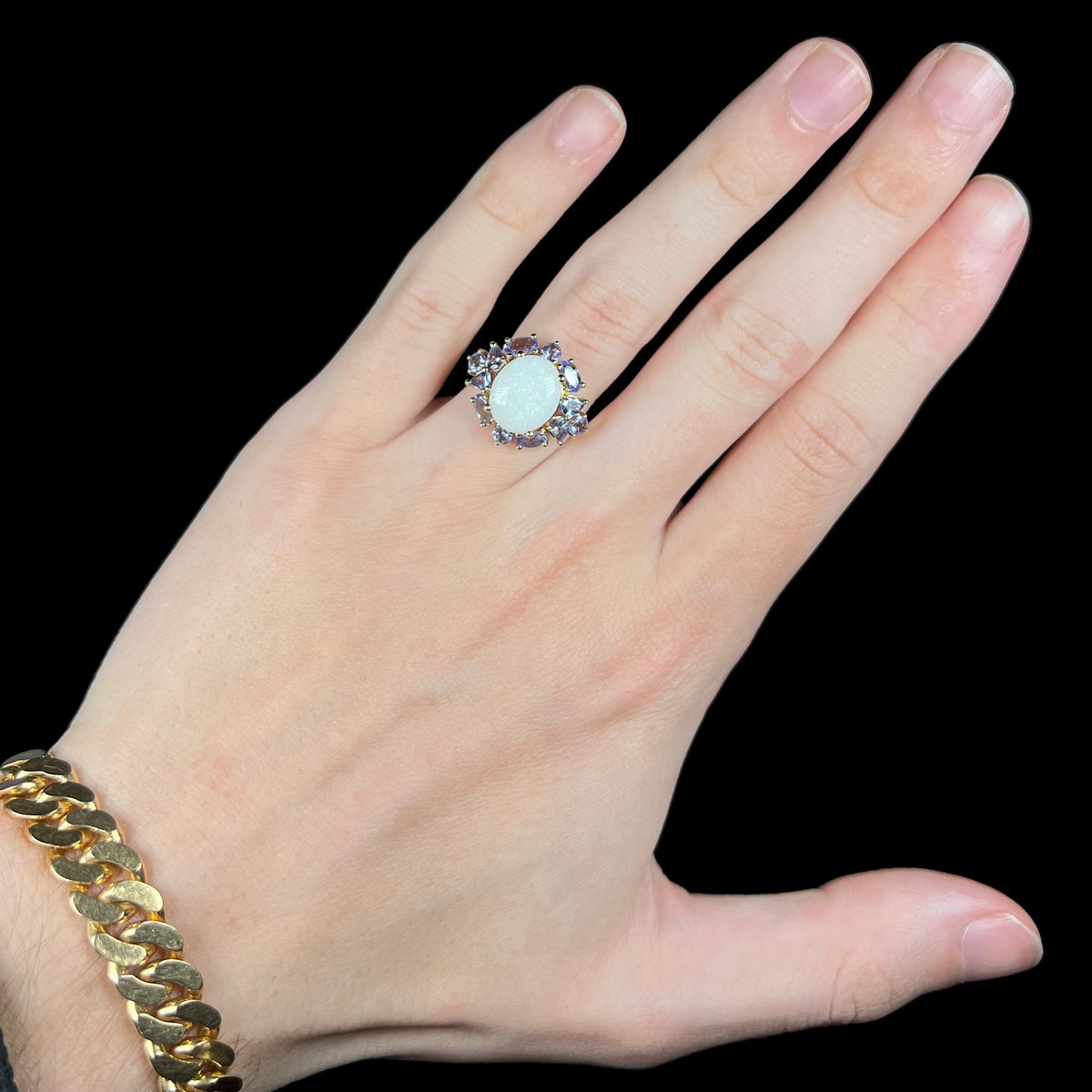 Hand wearing an Australian opal and tanzanite-accented women's ring in 14k gold under cool LED studio lights