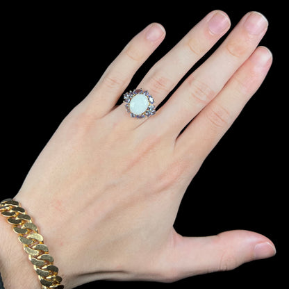 Hand wearing an Australian opal and tanzanite-accented women's ring in 14k gold under cool LED studio lights