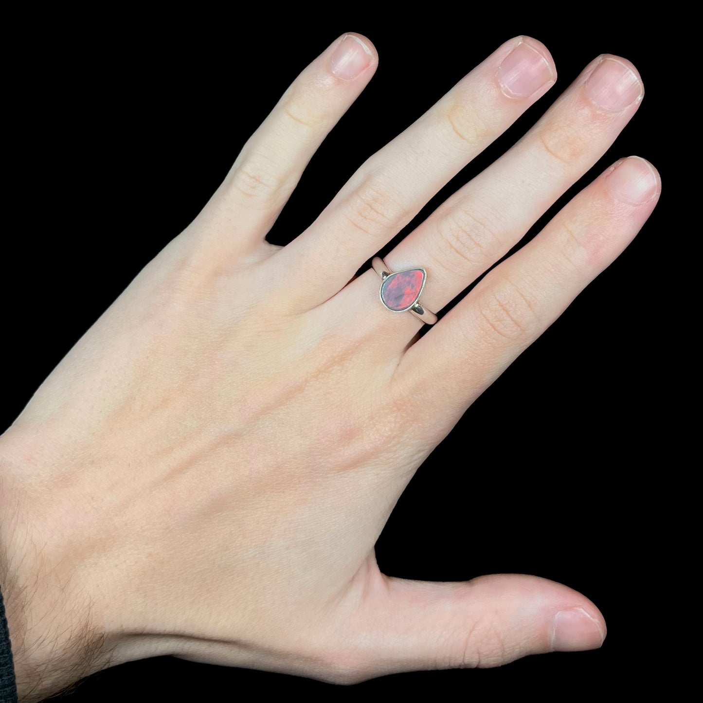 Hand wearing a women's sterling silver pear shaped Australian opal ring.  A red flash of color is seen under LED studio lights.