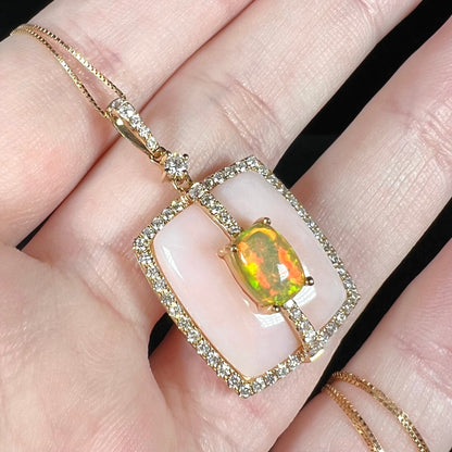 Angled close-up of a women's pink opal and fire opal diamond halo pendant necklace in 14k gold, held in a hand.
