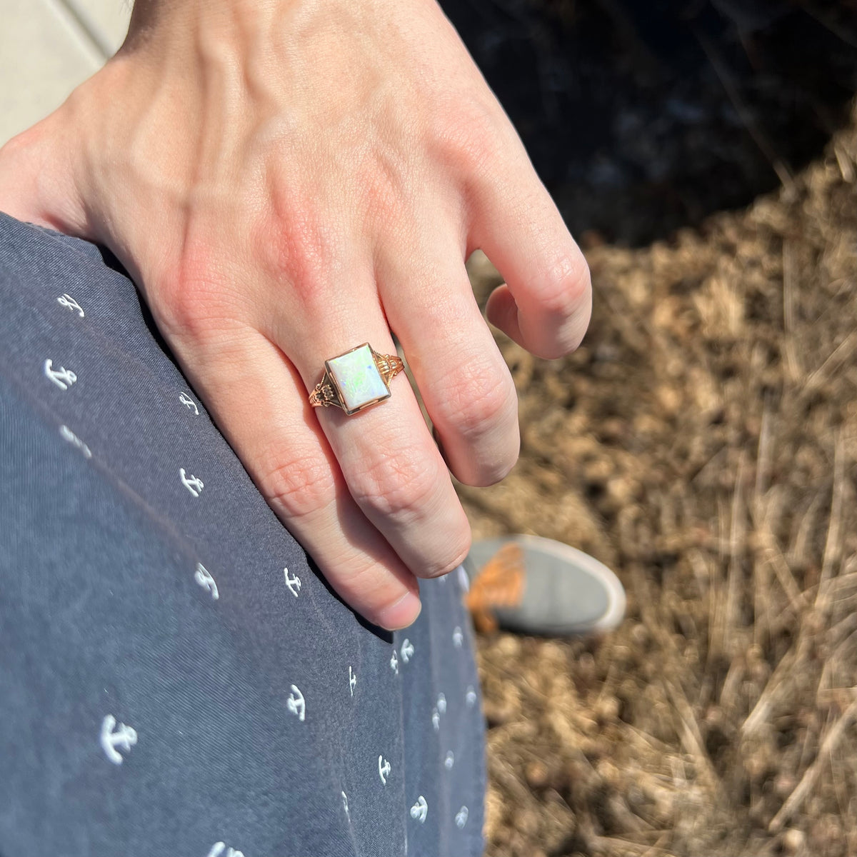Close-up of person resting hand on hip in sunlight wearing an antique women's rectangle-shaped Australian opal solitaire ring