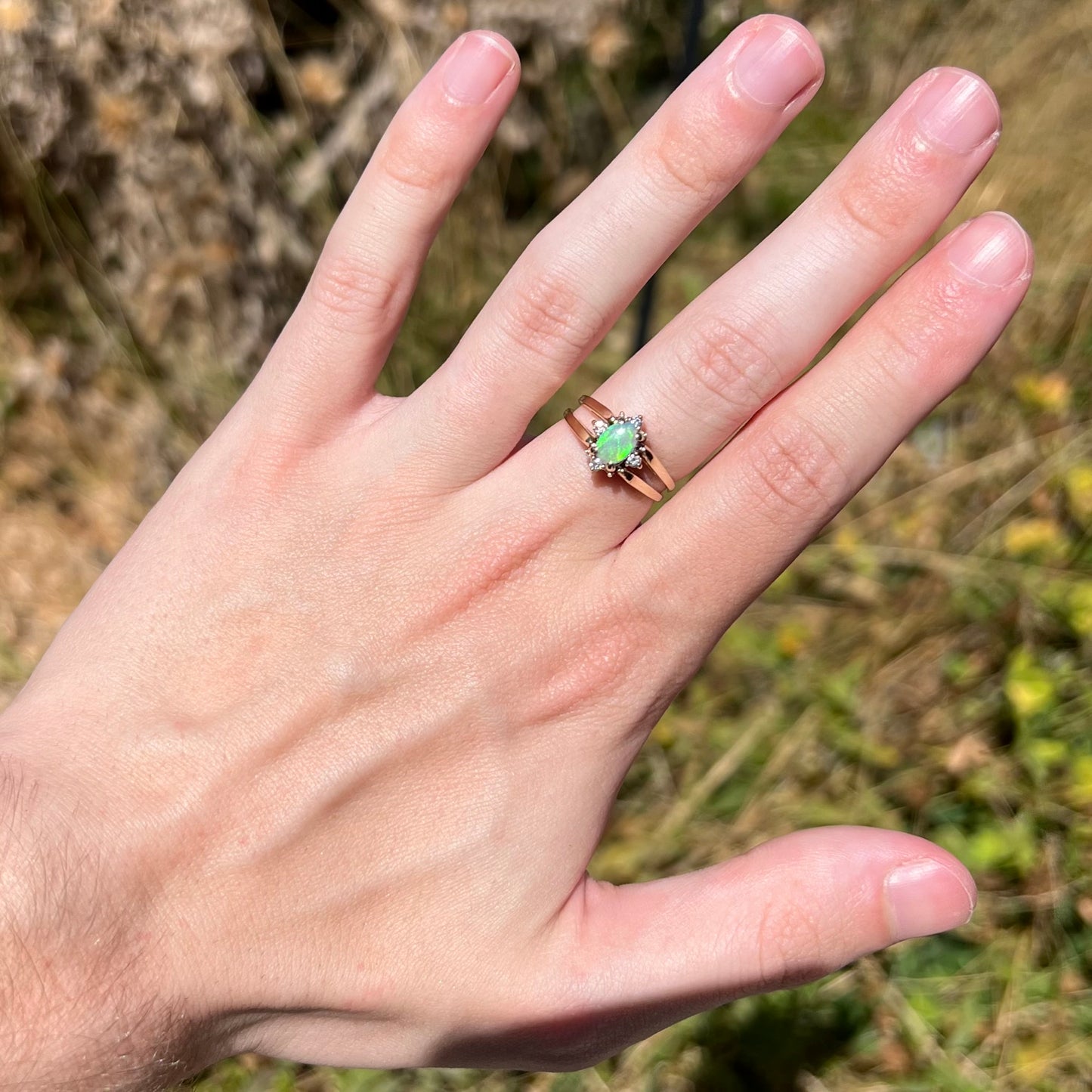 Hand wearing women's reversible gold opal and diamond ring in sunlight