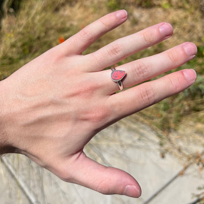 Hand wearing a women's sterling silver Australian opal ring that shows a bright, full red flash of color in the natural sunlight.