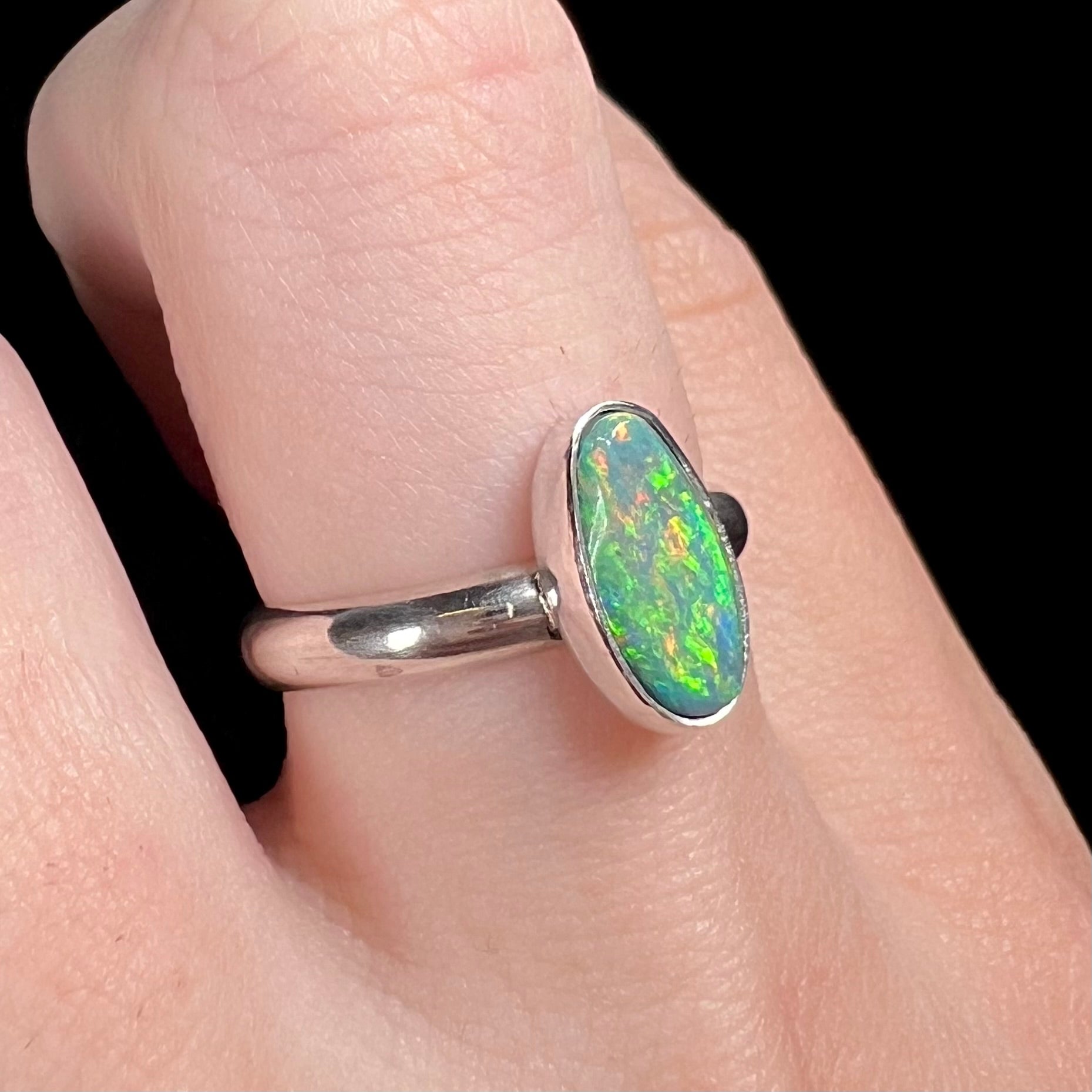 A women's sterling silver Australian opal solitaire ring with green play of color, worn on a finger and shown from an angle.