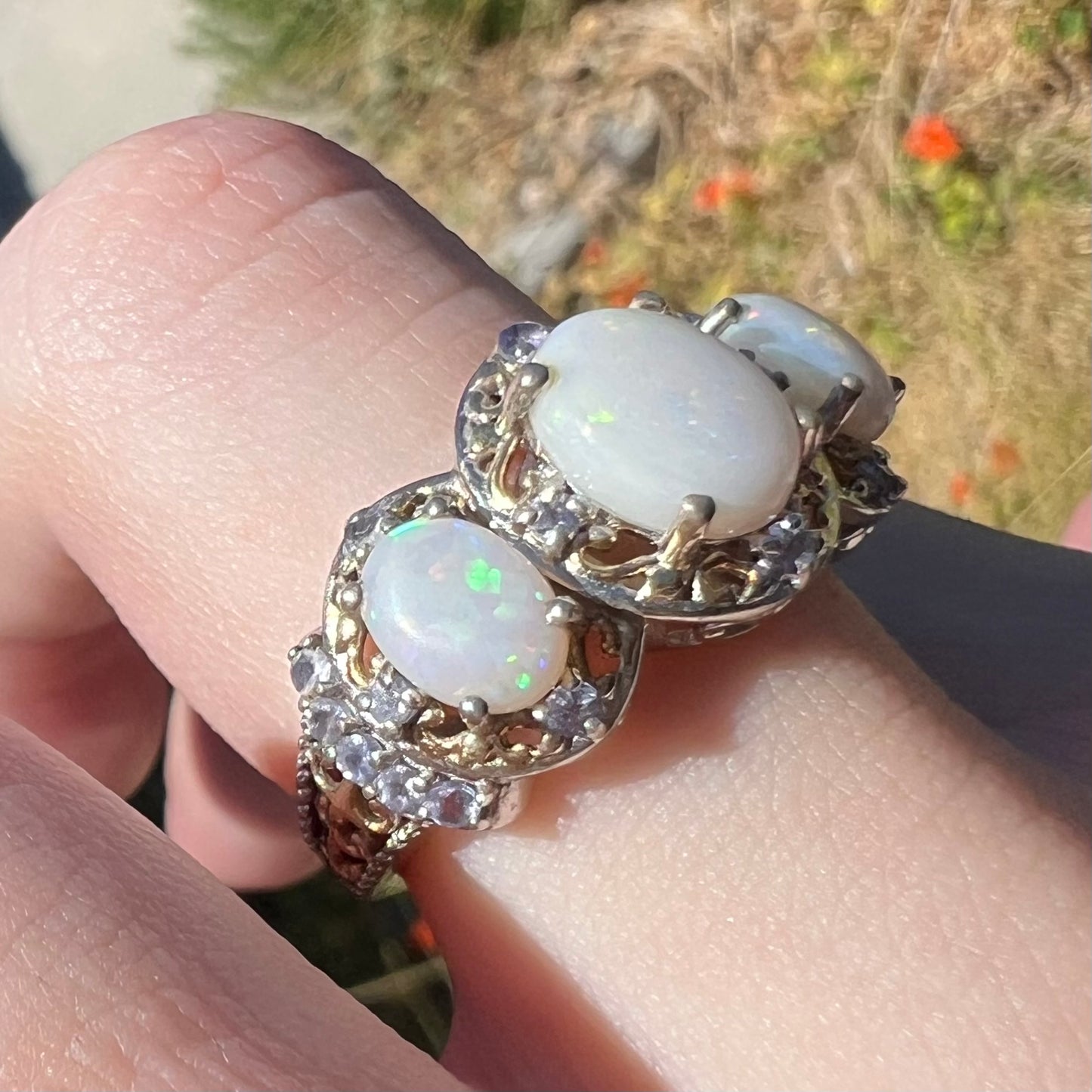 Macro view of a women's sterling silver Australian opal and tanzanite-accented filigree halo design ring, shown on a finger from an angle in natural light.