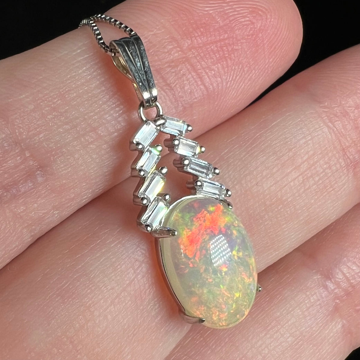 Women's silver Ethiopian opal and cubic zirconia pendant shown close-up in hand