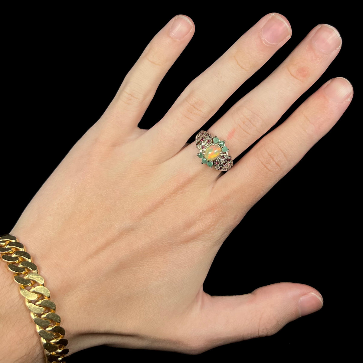 Hand wearing women's sterling silver Ethiopian opal ring with garnet and emerald accents
