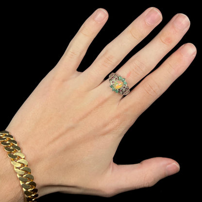 Hand wearing women's sterling silver Ethiopian opal ring with garnet and emerald accents