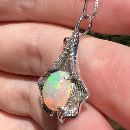 Women's sterling silver Ethiopian opal pendant with Chinese leaf design, held in hand under natural light