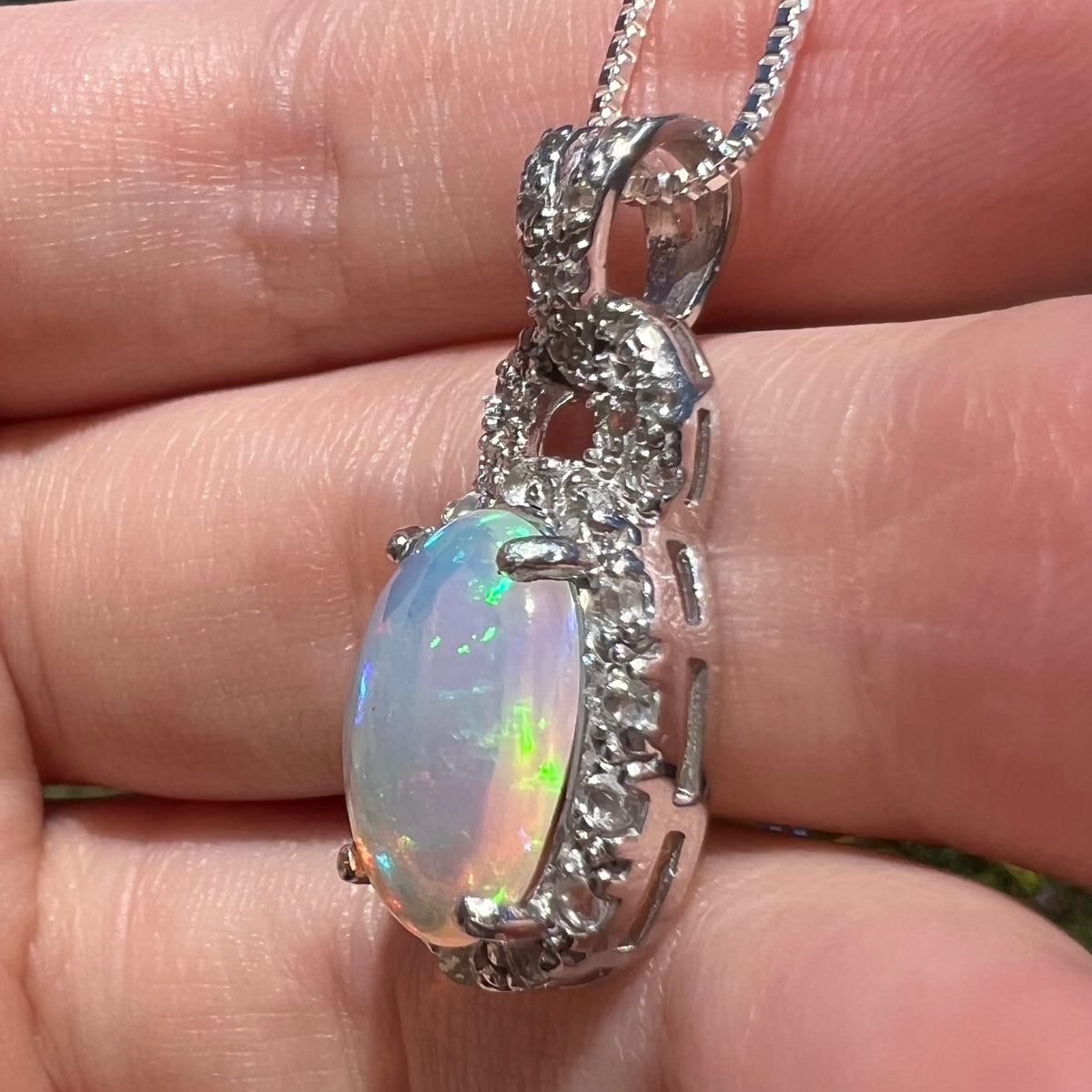 Side view of women's silver Ethiopian opal halo design pendant, held in hand under sunlight