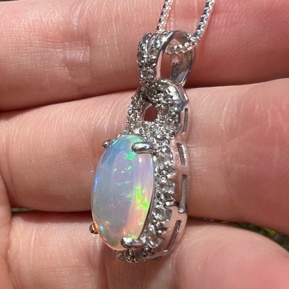 Side view of women's silver Ethiopian opal halo design pendant, held in hand under sunlight