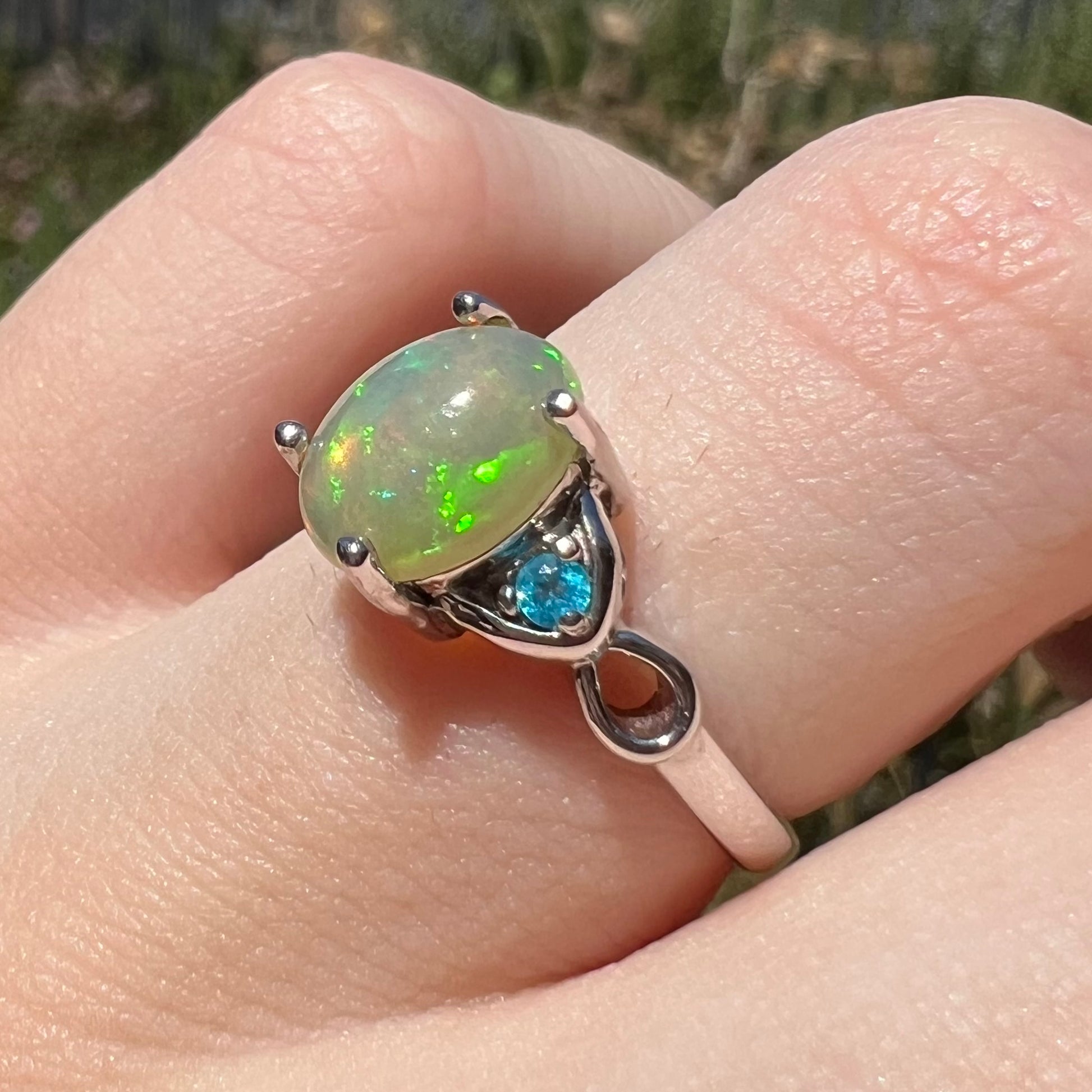 Angled close-up of women's silver Ethiopian opal ring with apatite accent in sunlight on finger
