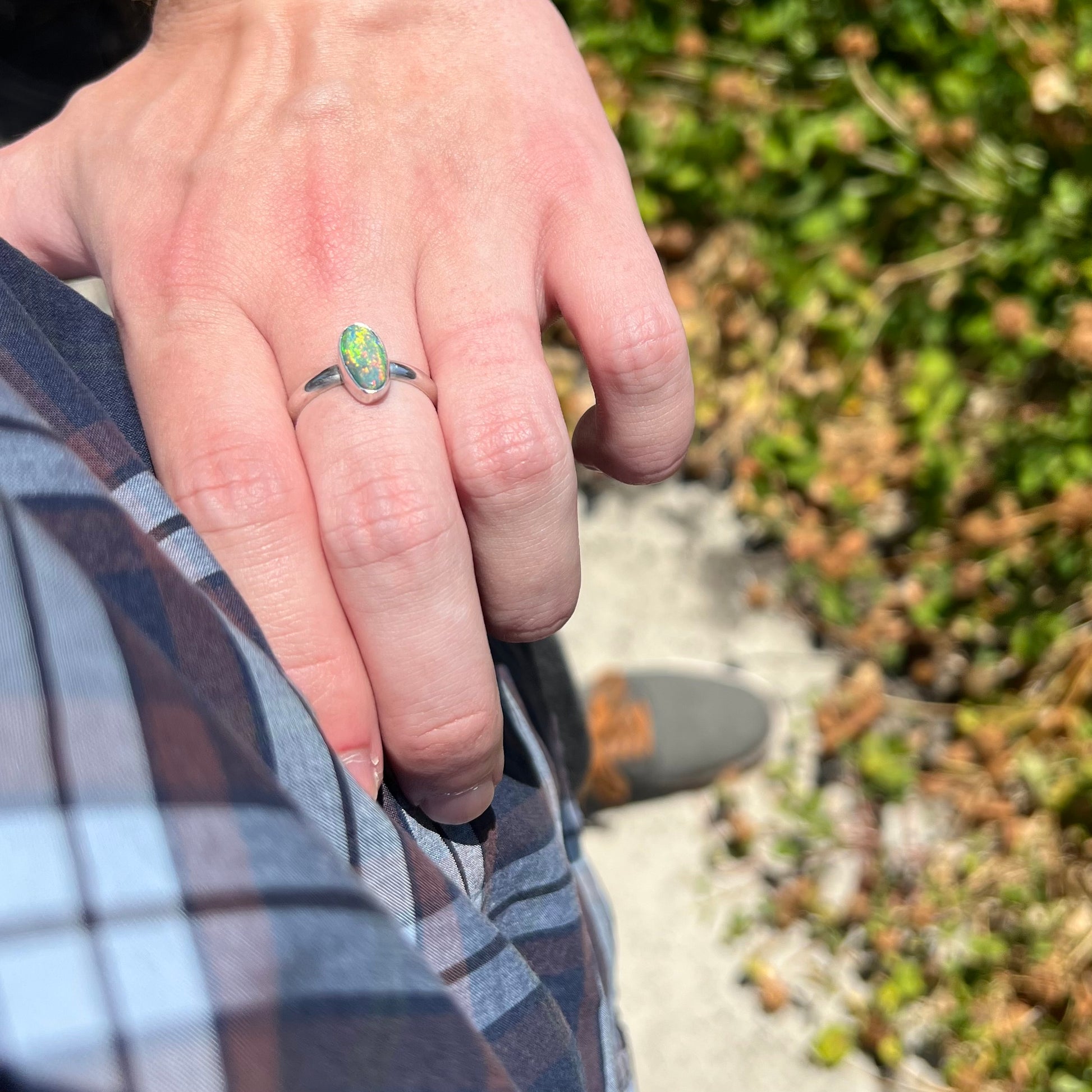 Person's hand resting on their hip in sunlight while wearing a women's sterling silver Australian opal solitaire ring with multicolor fire.