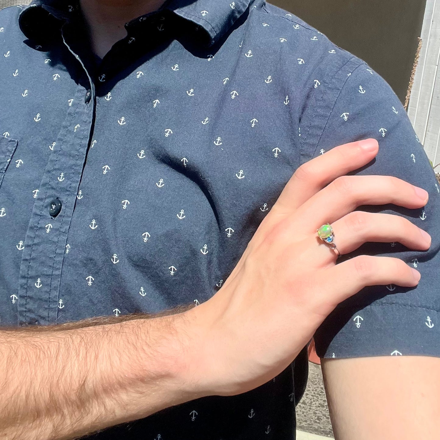Person resting hand on shoulder while wearing sterling silver Ethiopian opal and blue apatite ring in sunlight
