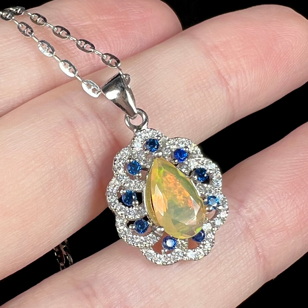 Women's sterling silver fire opal and blue sapphire necklace with anchor style chain, shown close-up held in hand