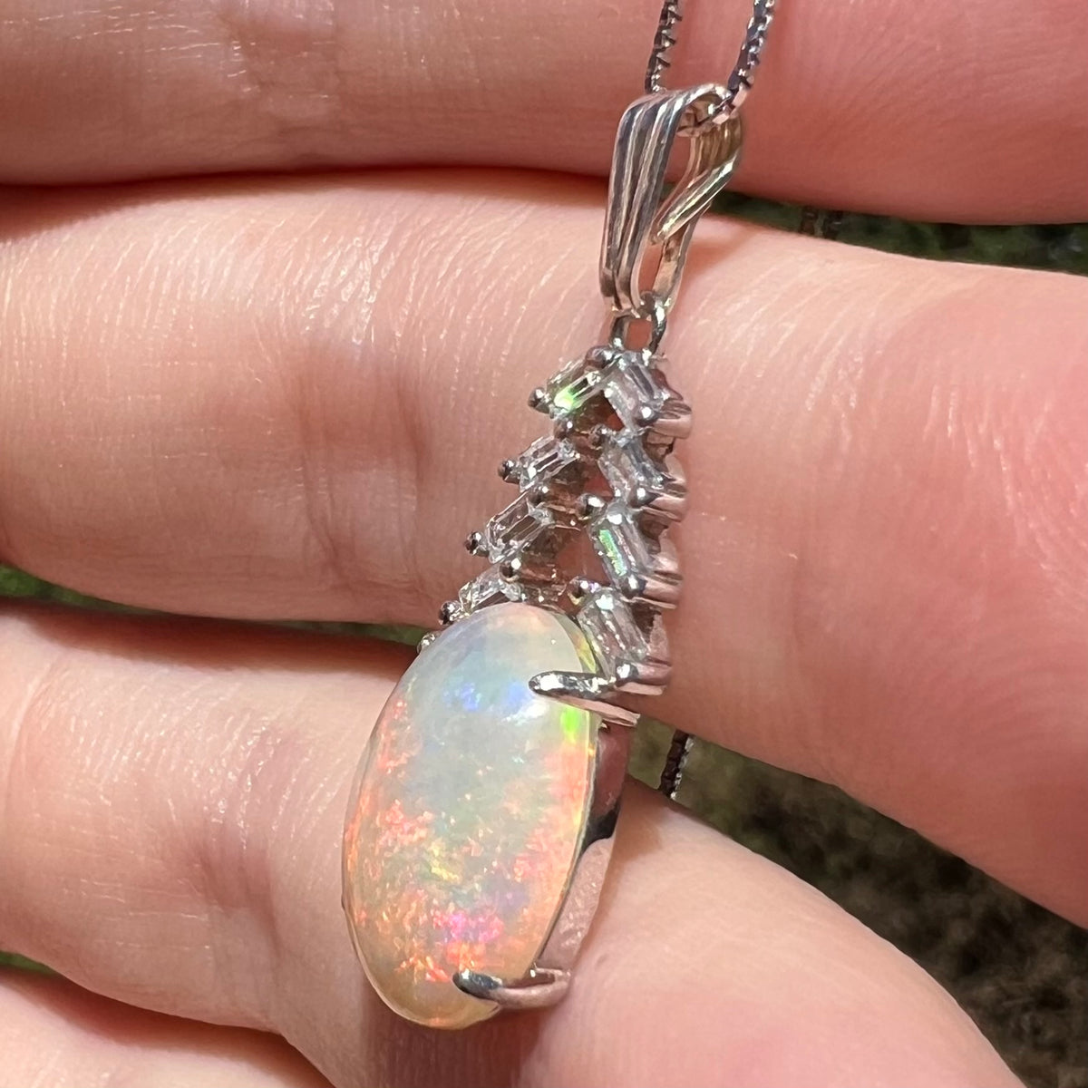 Women's sterling silver opal and emerald cut CZ drop pendant, held in hand under sunlight
