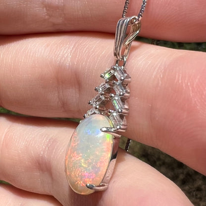 Women's sterling silver opal and emerald cut CZ drop pendant, held in hand under sunlight