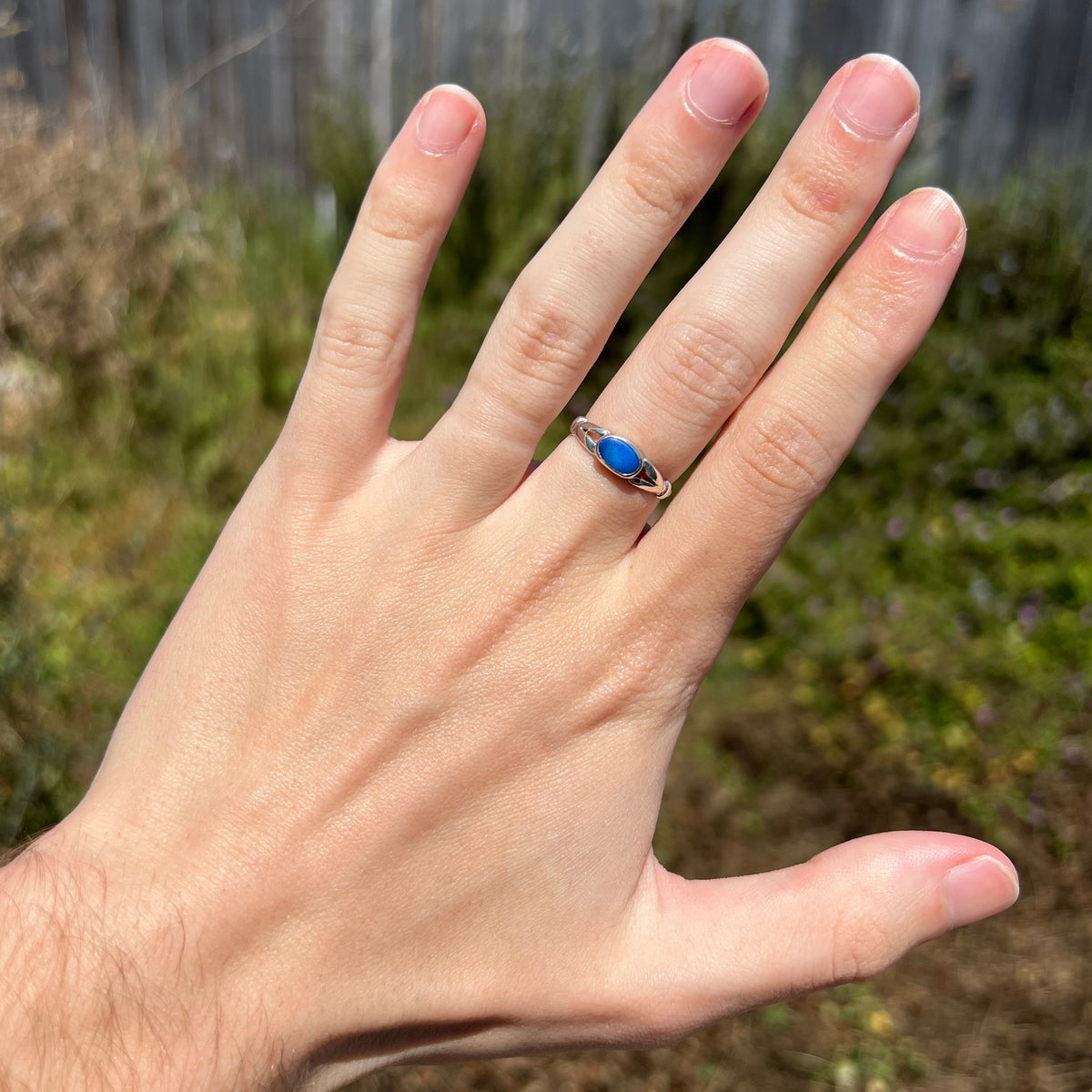 Hand wearing women's silver opal doublet ring in natural light against outdoor background