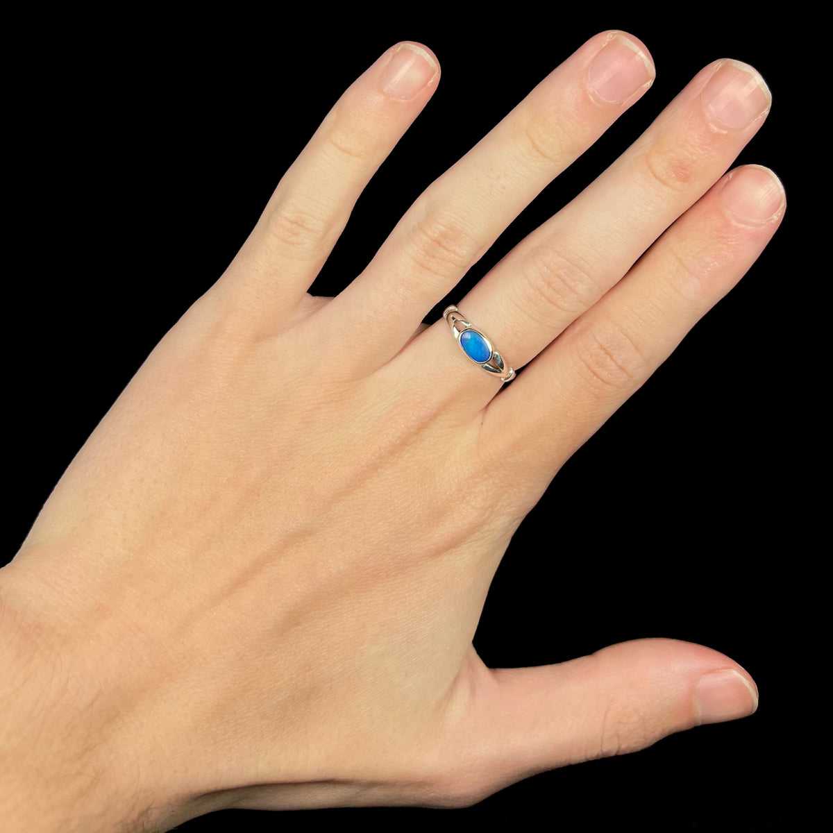 Hand wearing women's horizontally mounted blue opal doublet ring with sterling silver split shank design