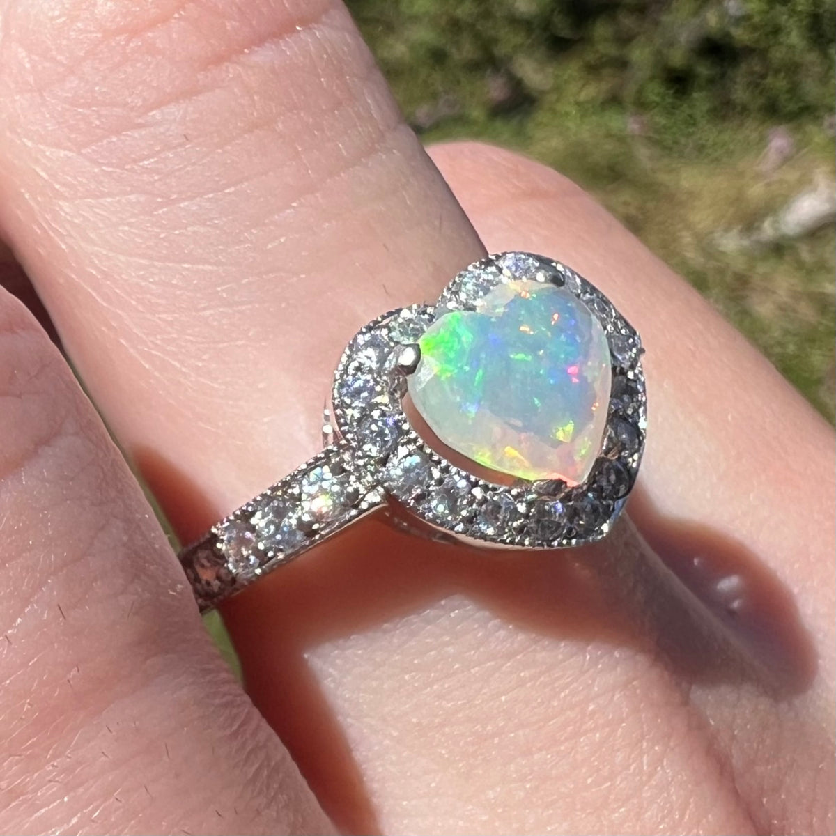 Close-up sunlit angled view of women's sterling silver opal heart ring with cubic zirconia accents, worn on finger
