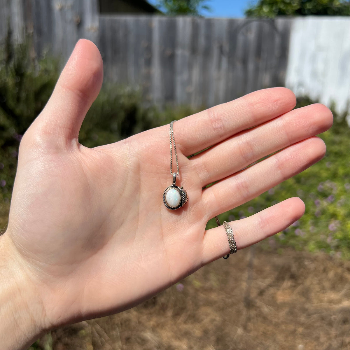 Women's sterling silver Southwest design opal necklace with feather design, held in hand under sunlight