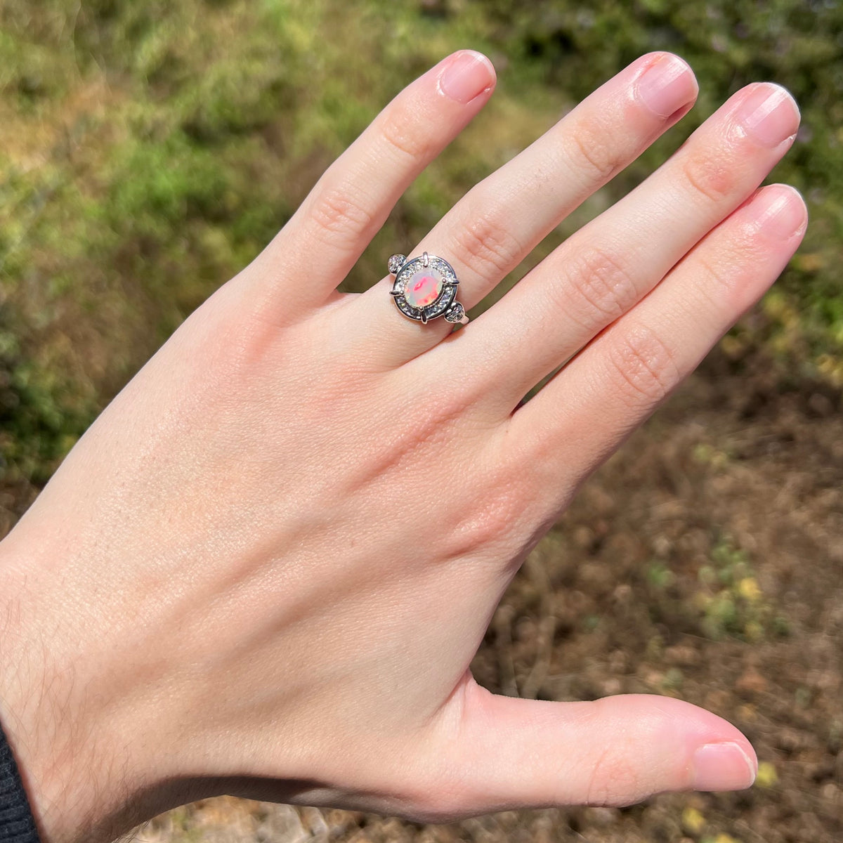 Hand wearing women's sterling silver Ethiopian opal ring with red flash of color in natural sunlight
