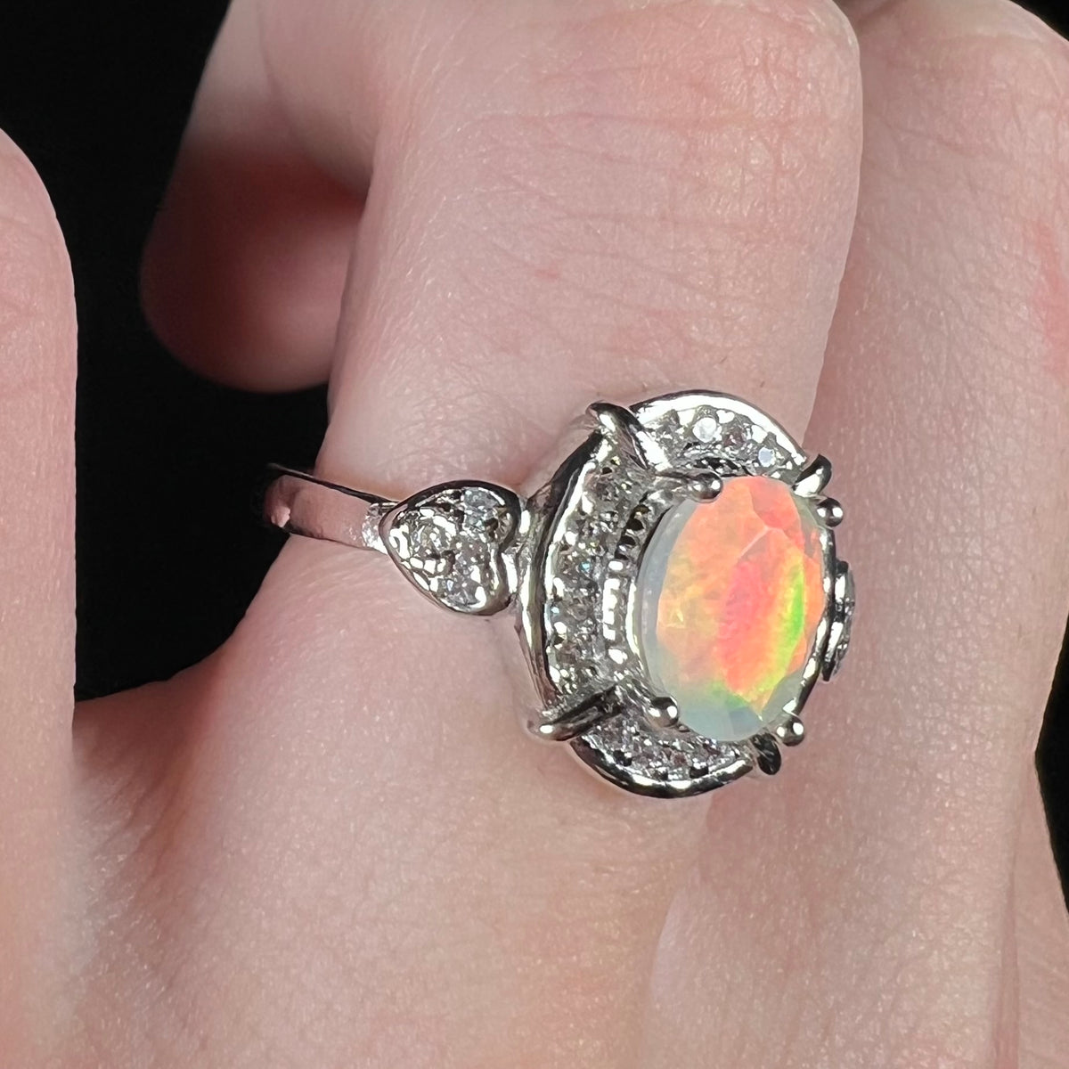 Red and green flash seen on Ethiopian opal mounted in women's sterling silver healo and heart design ring, worn on finger