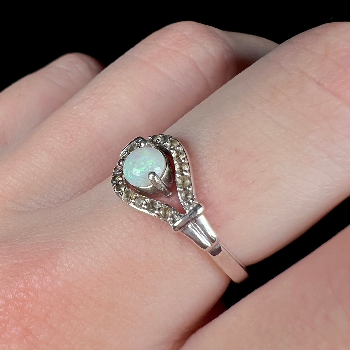 Angled close-up of women's sterling silver opal and smoky quartz-accented ring, worn on finger