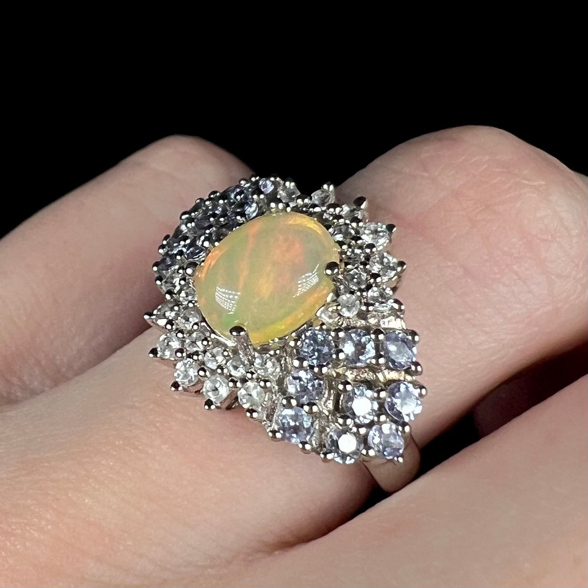 Angled close-up of women's sterling silver opal, white topaz, and tanzanite ring, worn on finger
