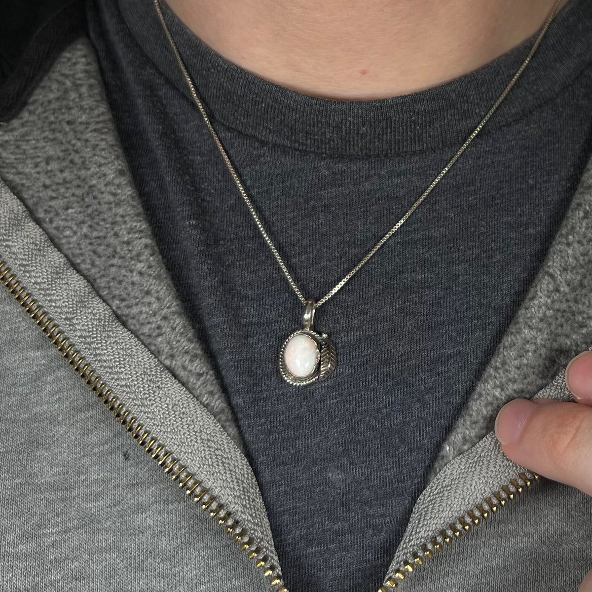 Close-up of person's neck and chest wearing a women's sterling silver white opal necklace with Southwest-inspired leaf design against a dark shirt