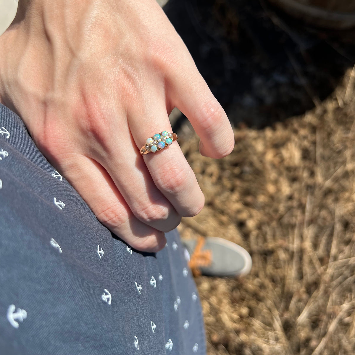 Person's hand resting on hip in sunlight wearing women's Victorian era six-stone opal ring with four seed pearl accents