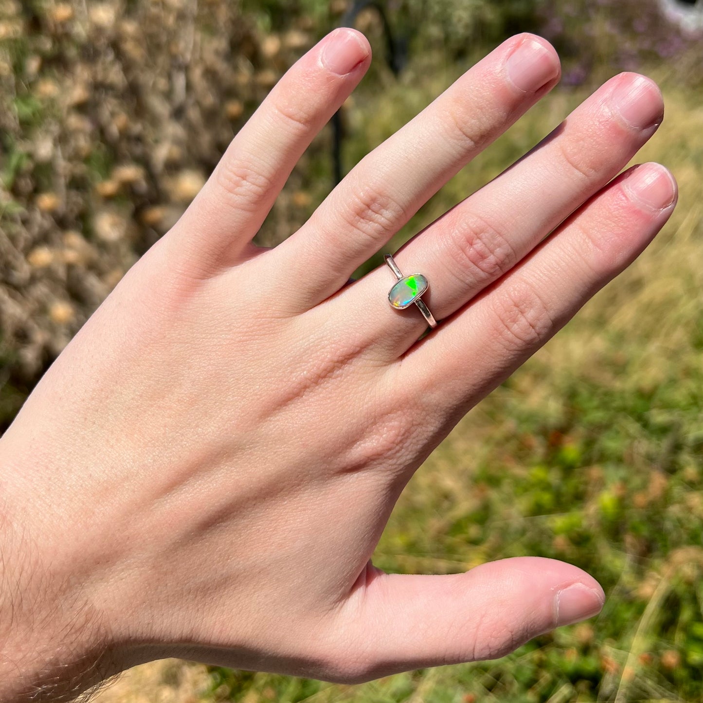 Hand wearing a women's sterling silver Australian crystal opal ring in natural sunlight.  The opal shows a flash of green.