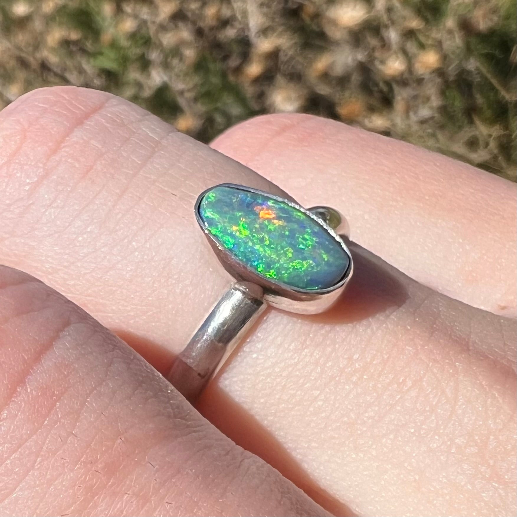 A women's sterling silver Australian opal solitaire ring, shown from an angle close-up on a finger in natural light.
