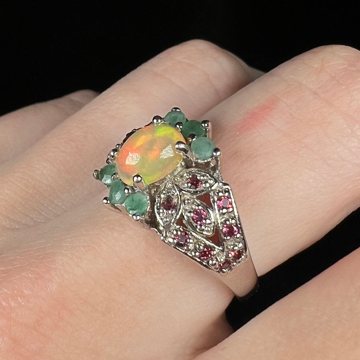 Macro angled view of women's sterling silver Ethiopian opal, garnet, and emerald ring worn on finger