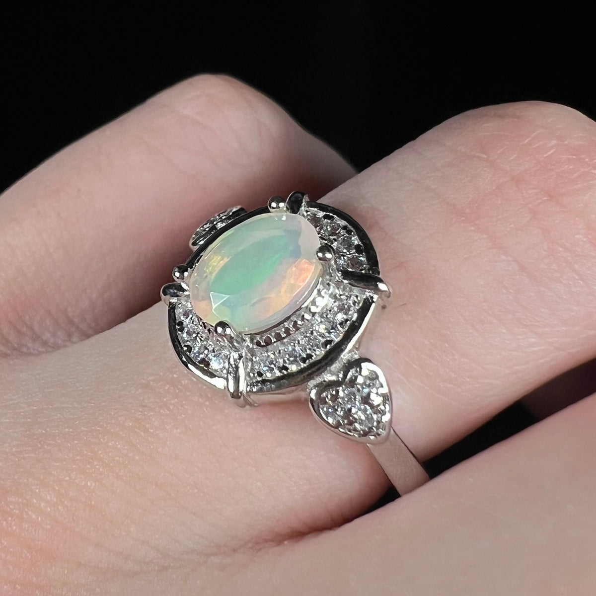 Women's sterling silver faceted Ethiopian opal ring worn on finger, showing CZ-accented heart designs